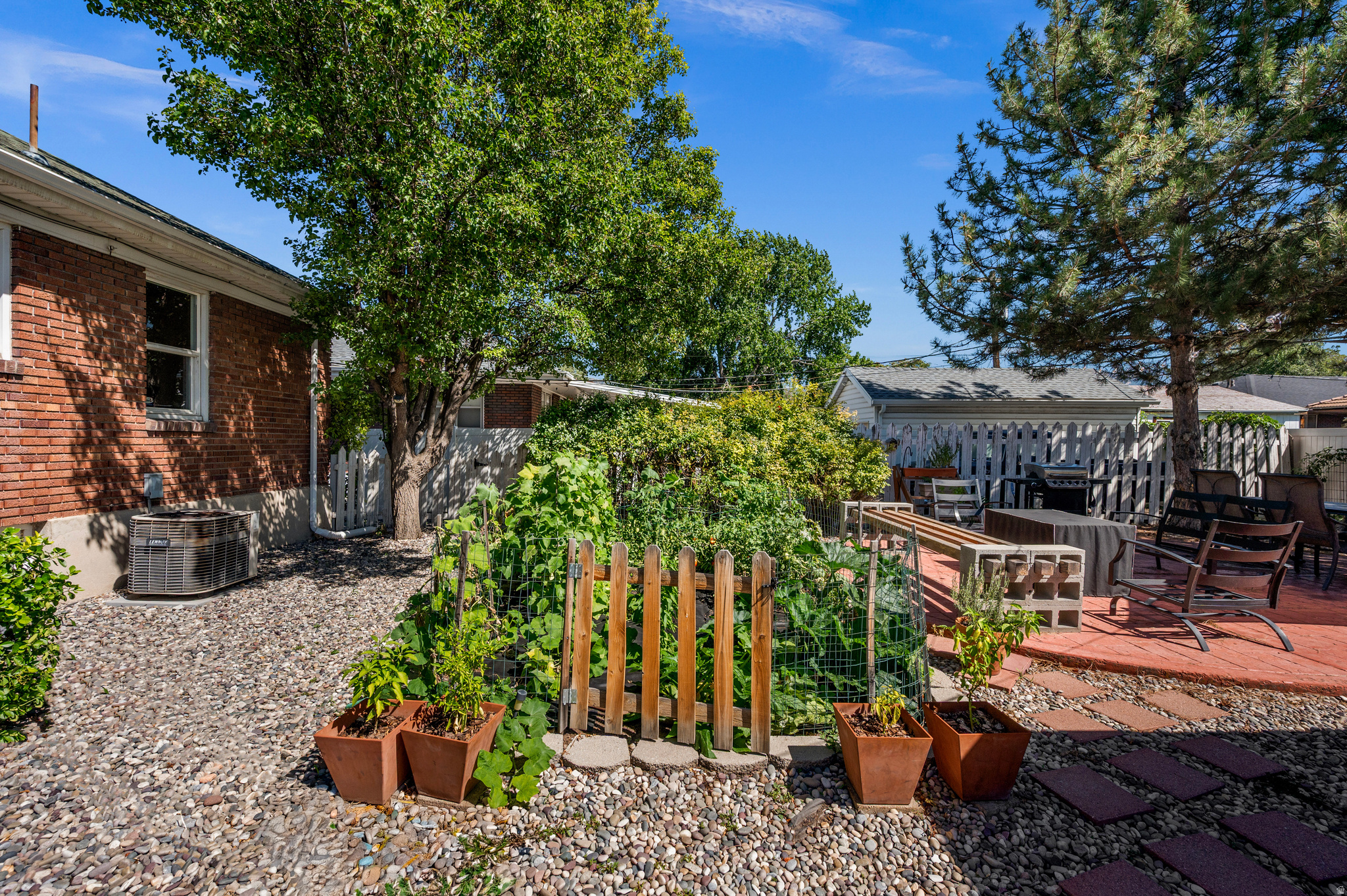 Backyard with a fenced vegetable garden, potted plants, and a furnished red patio.