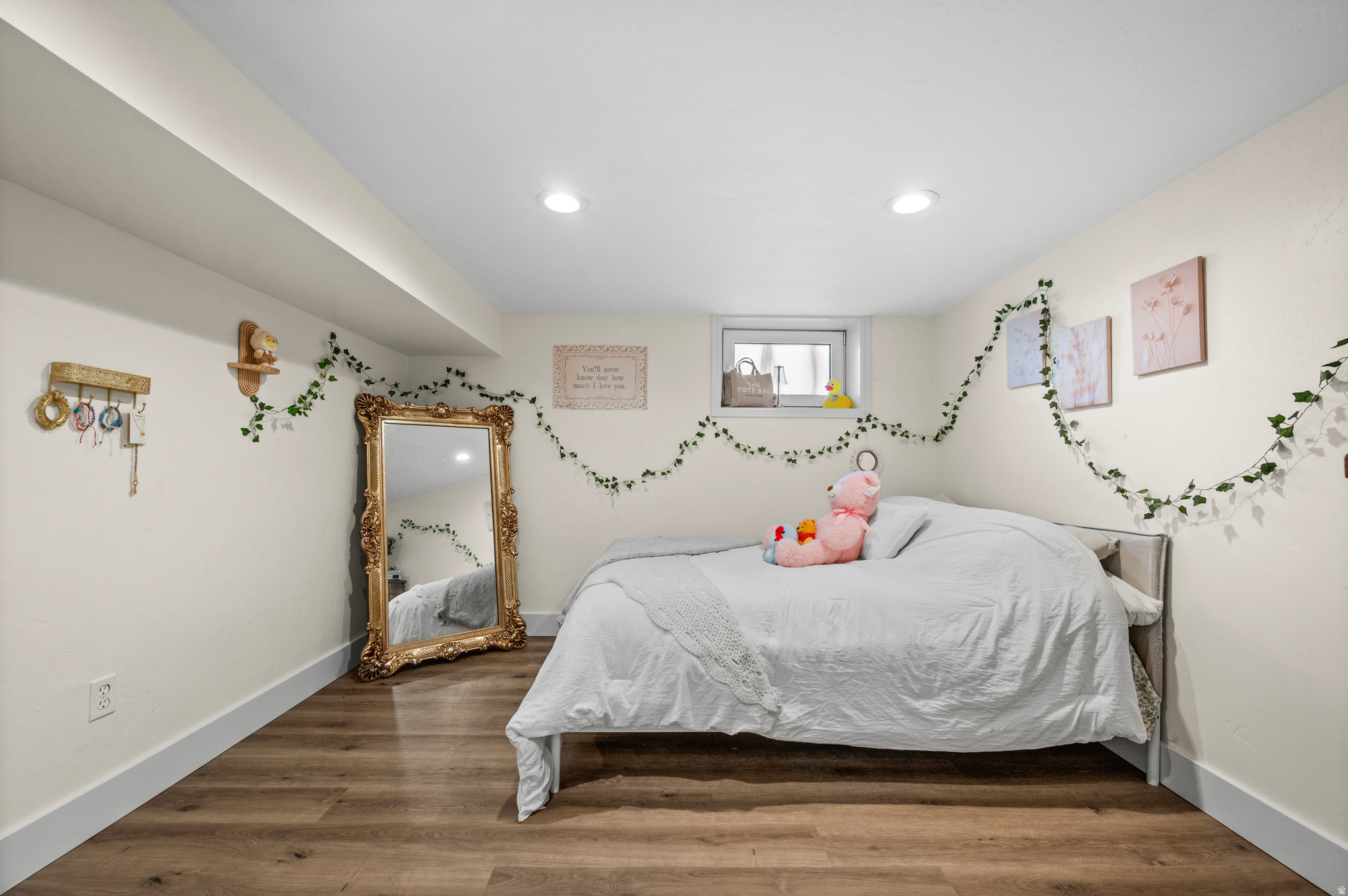 Bedroom with a white-covered bed, pink plush toy, ornate gold mirror, and ivy garlands.