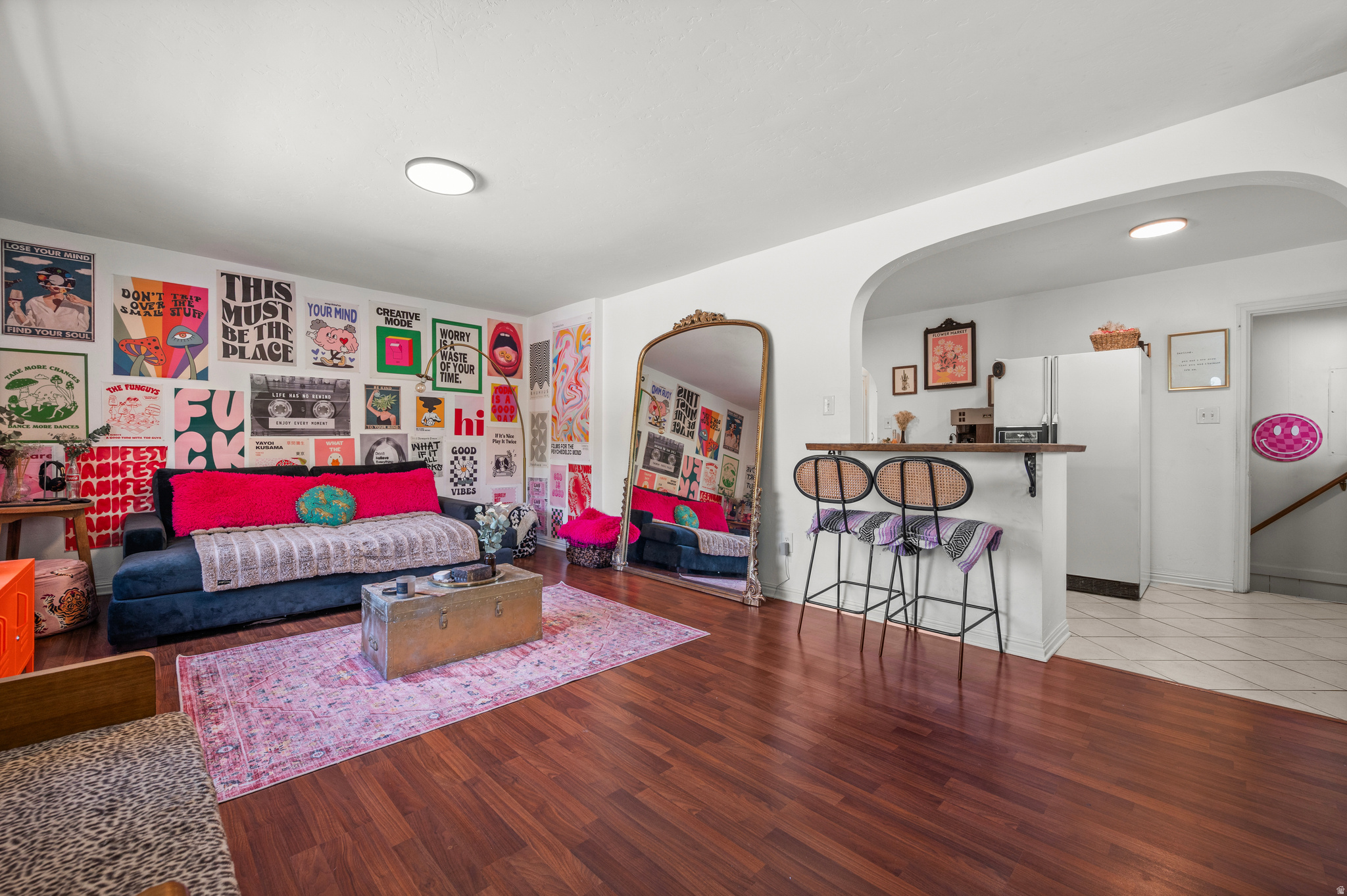 Living room with colorful poster wall, navy sofa, bright pink cushions, and an arched opening to the kitchen.