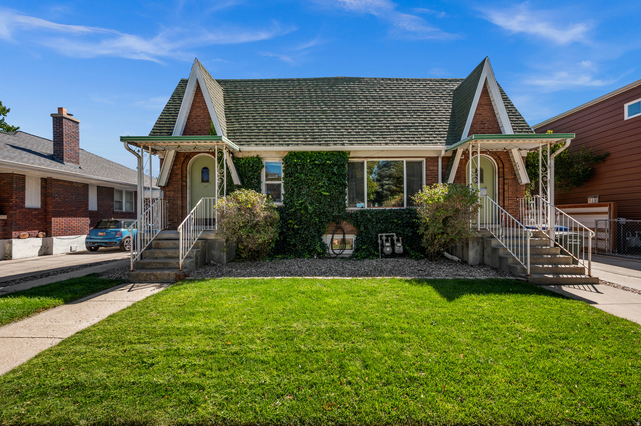 Brick duplex with twin gabled roofs, separate stairways, ivy-covered facade, and a green front lawn.
