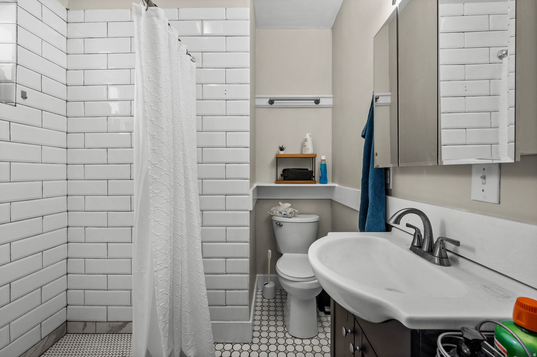 Bathroom with white subway tile, hexagonal mosaic flooring, a wide sink, and mirrored medicine cabinet.