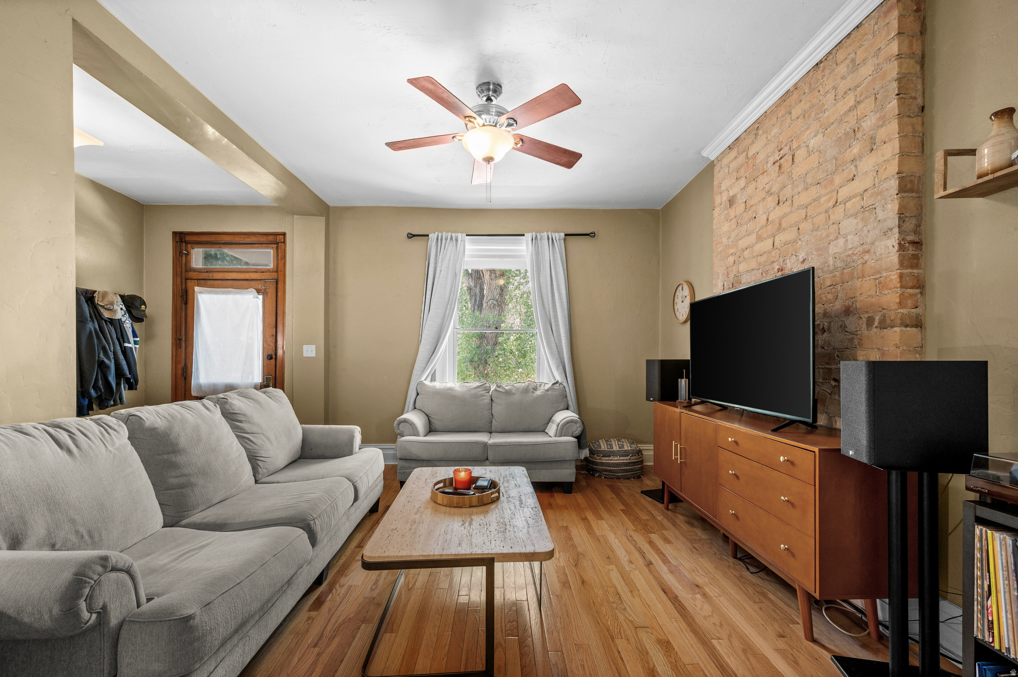 Living room with gray sofas, hardwood floors, and an exposed brick wall behind the television.