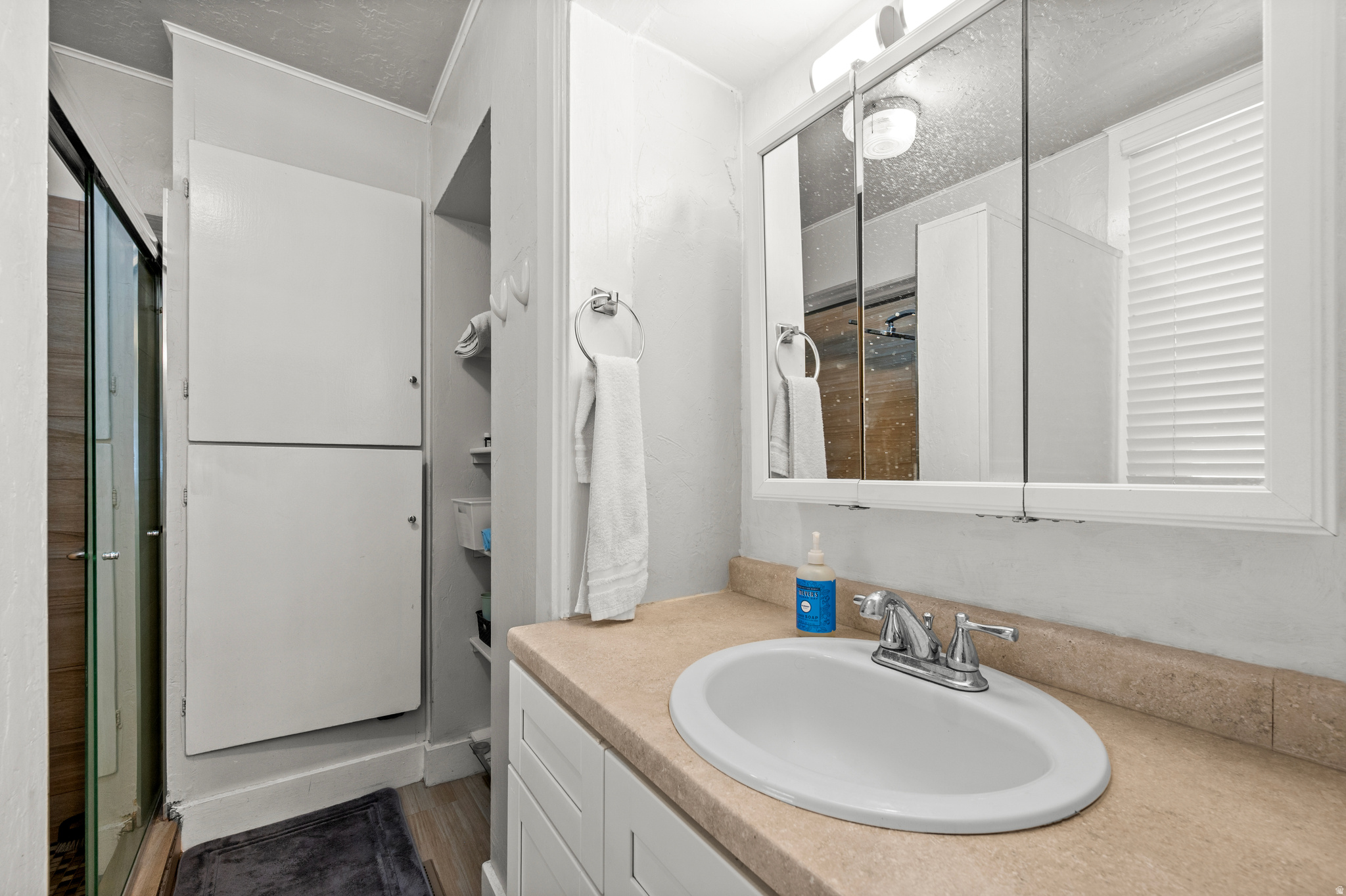 Bathroom vanity with oval sink and mirrored cabinet beside a glass shower.