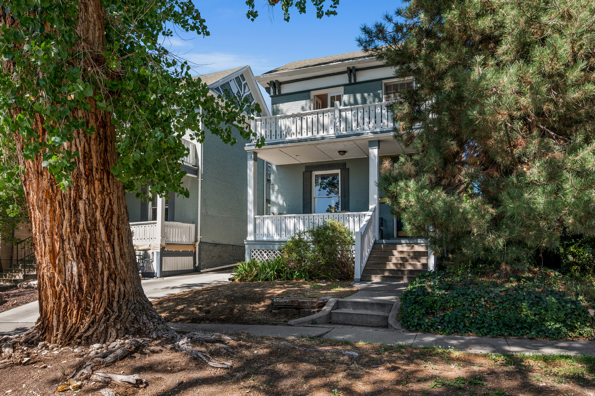 Blue-gray two-story home with white balconies, framed by large trees.