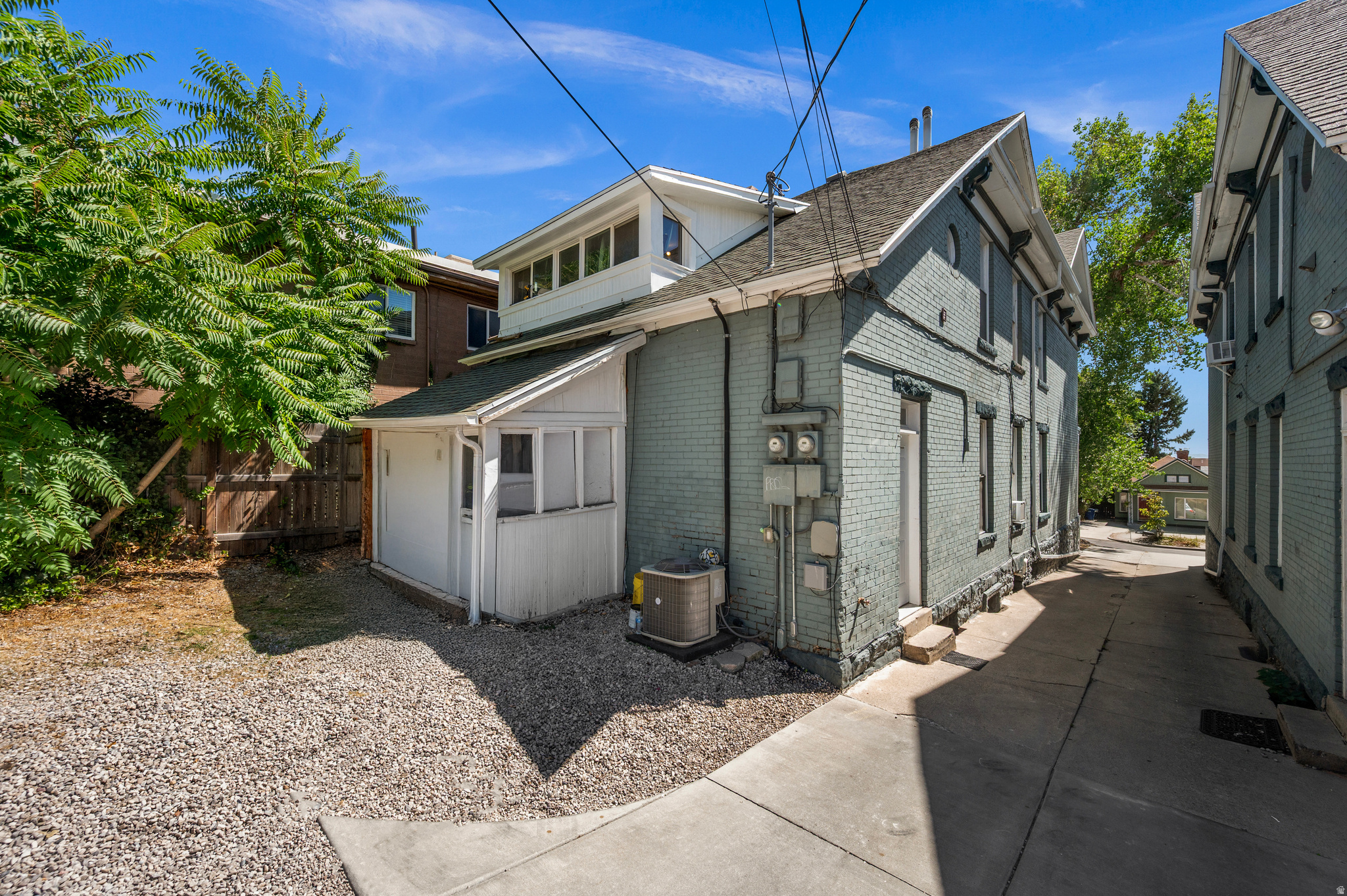 Gray brick house with a white enclosed porch beside a narrow driveway and gravel yard.