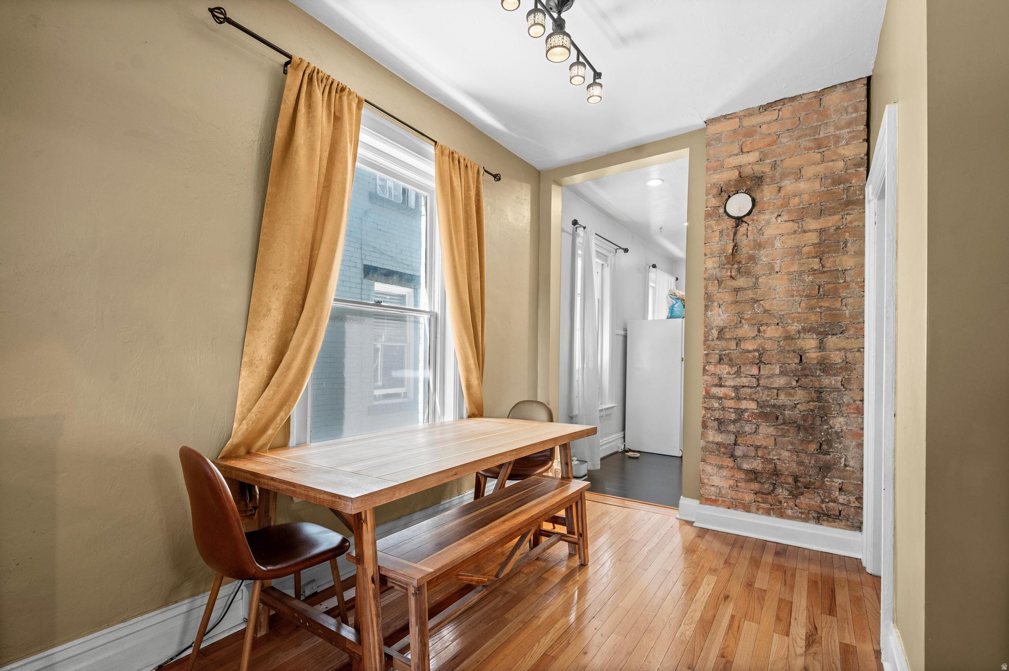 Dining area with a wooden table and bench beside a window and exposed brick wall.