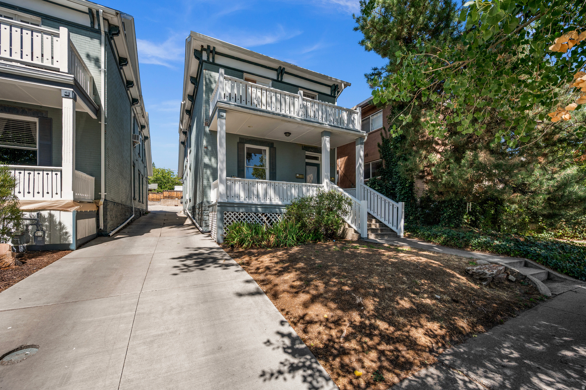 Gray-green home with white balconies and a covered porch beside a concrete driveway.