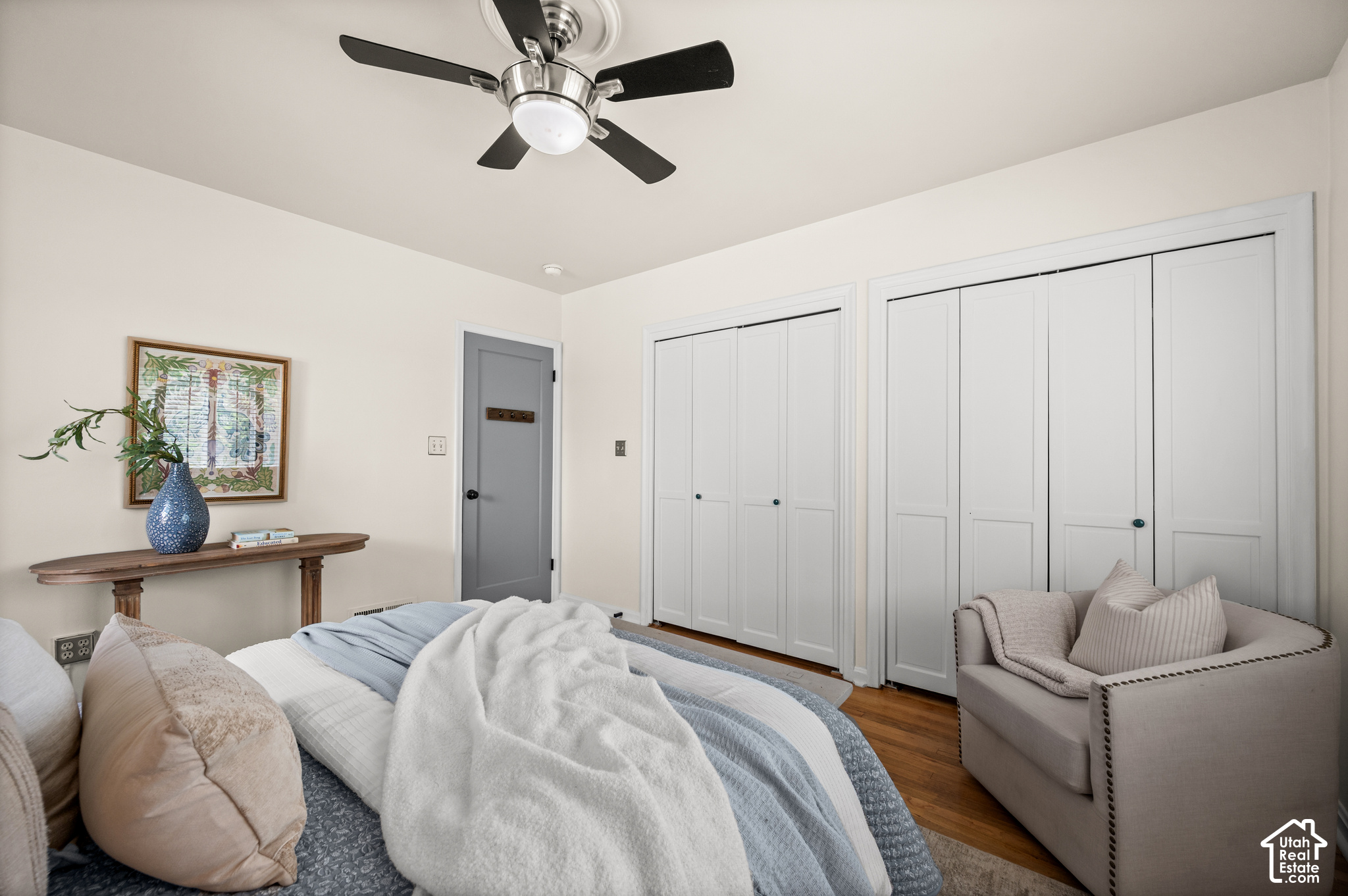 Staged bedroom with pale blue bedding, white closet doors, and a cushioned armchair.
