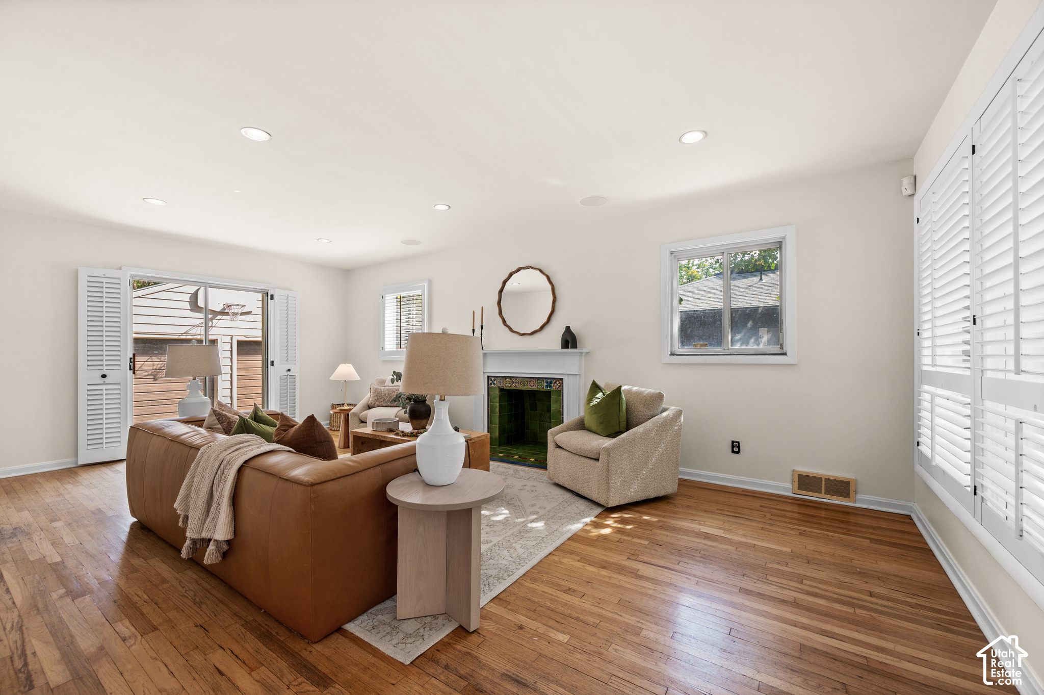 Staged living room with hardwood floors, a leather sofa, and a green-tiled fireplace.