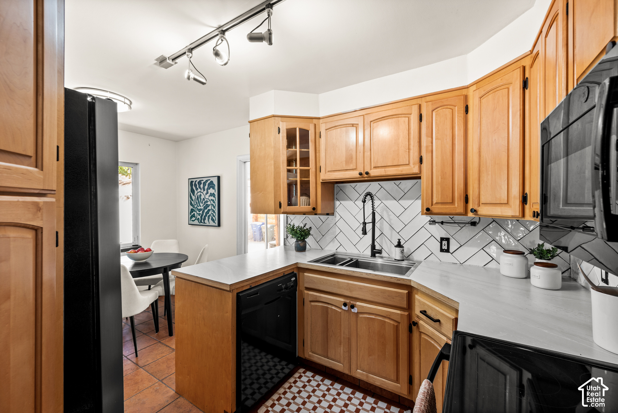 Kitchen with honey-colored cabinets, white counters, geometric tile backsplash, and an adjacent dining nook.