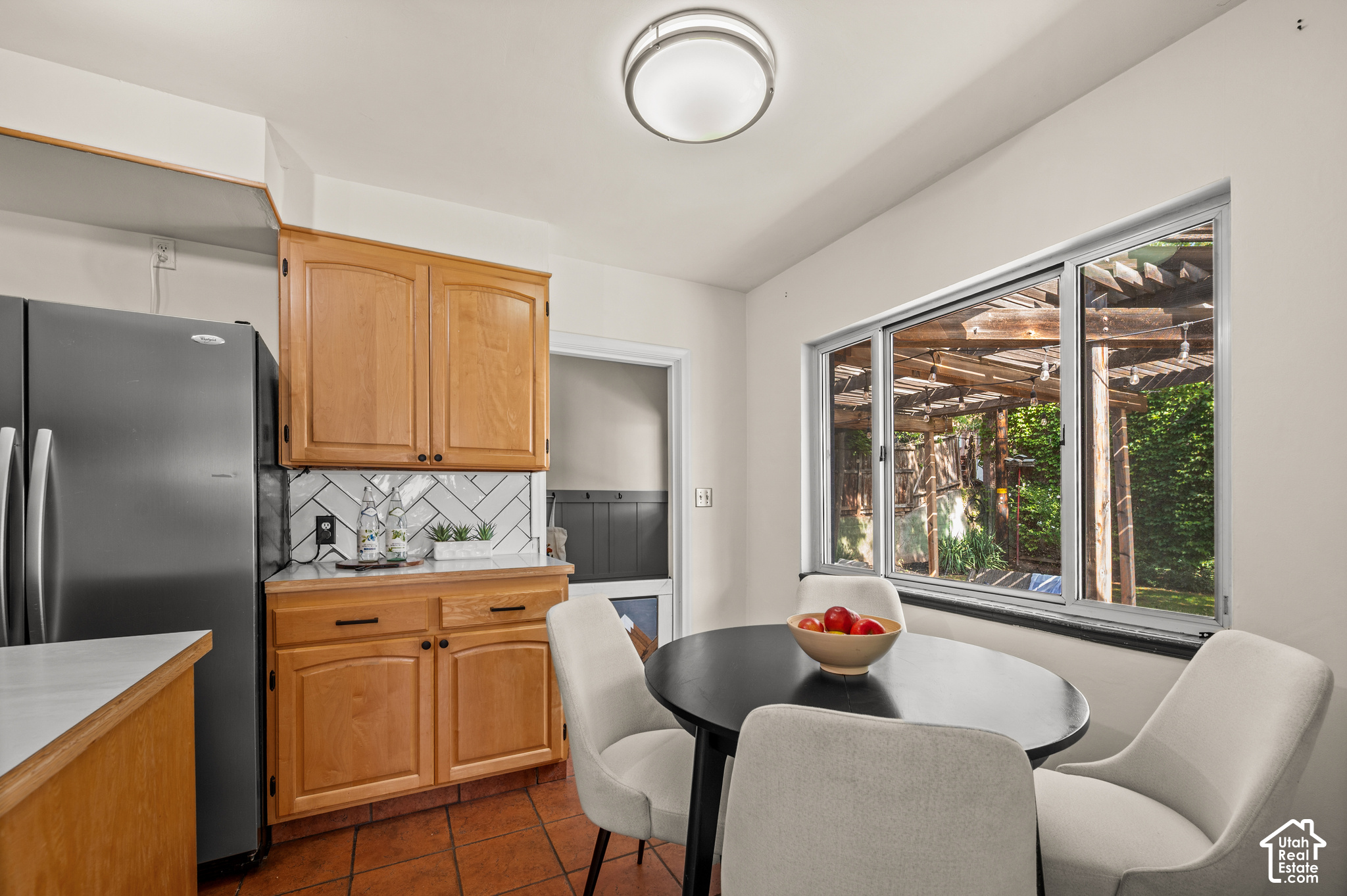 Kitchen dining area with wood cabinets, a round table, and a large window overlooking a pergola.