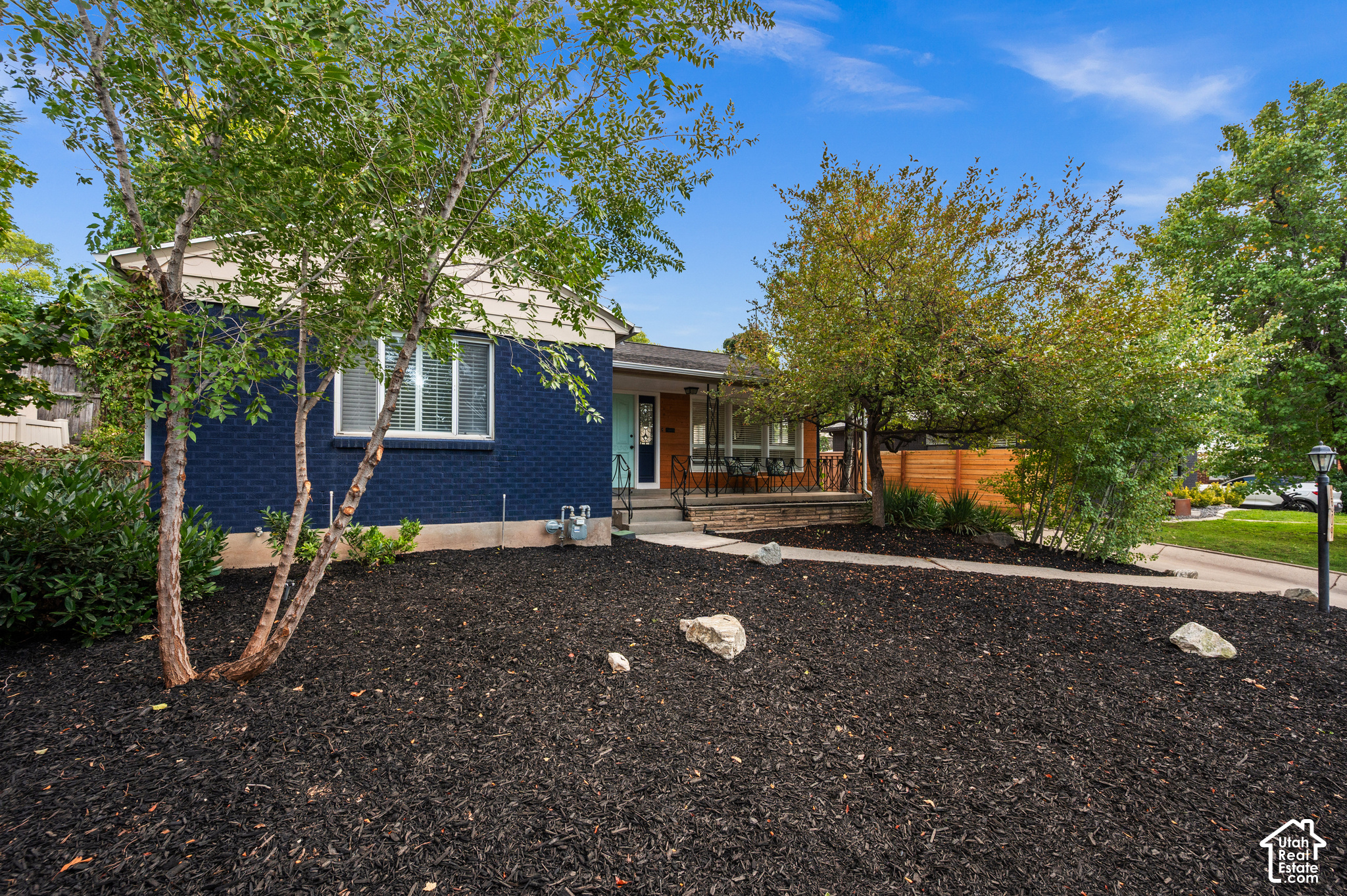 Single-story home with a dark blue brick facade, covered porch, and mature trees in the front yard.