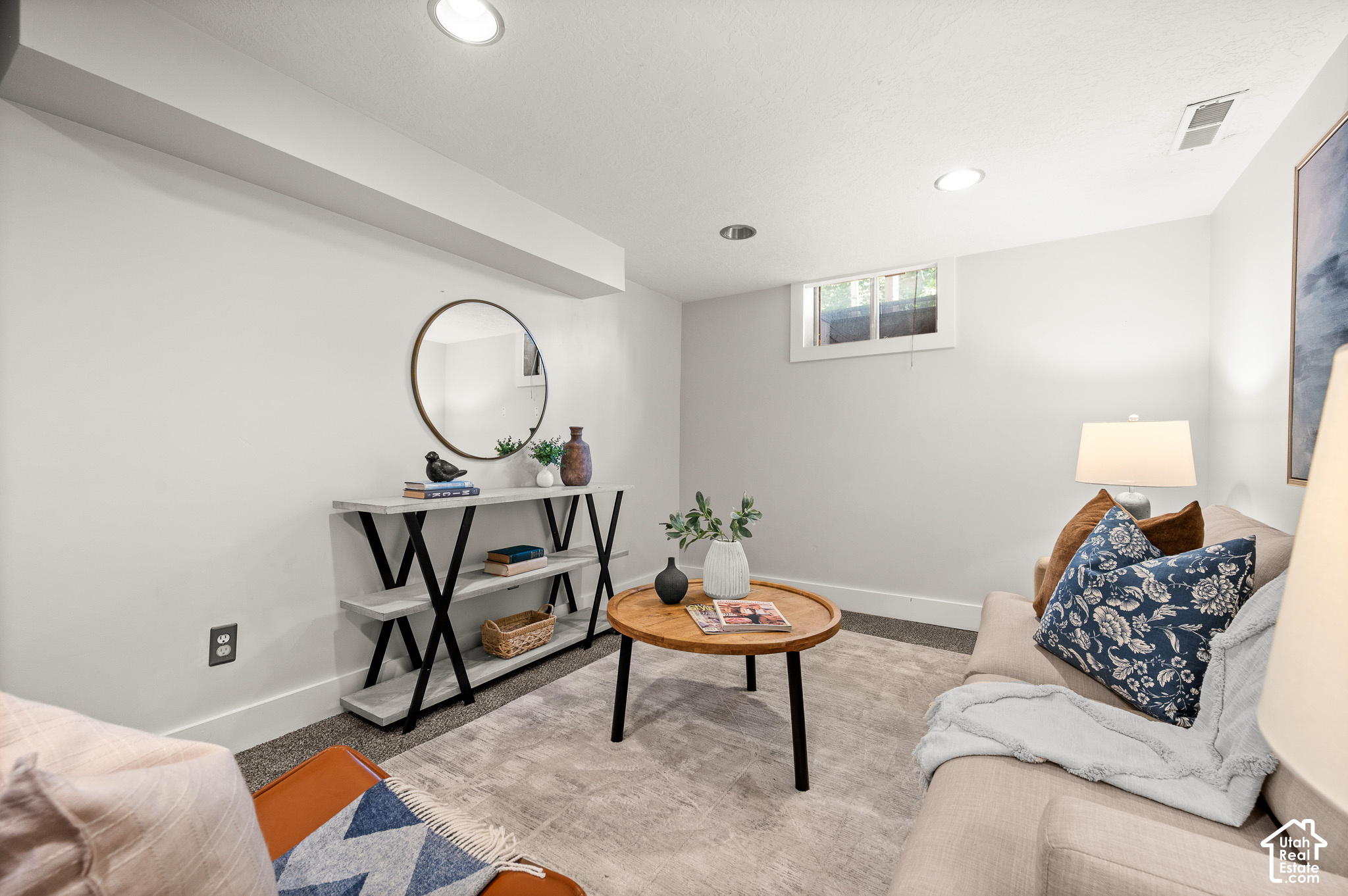 Staged basement sitting room with beige sofas, round coffee table, and high window.