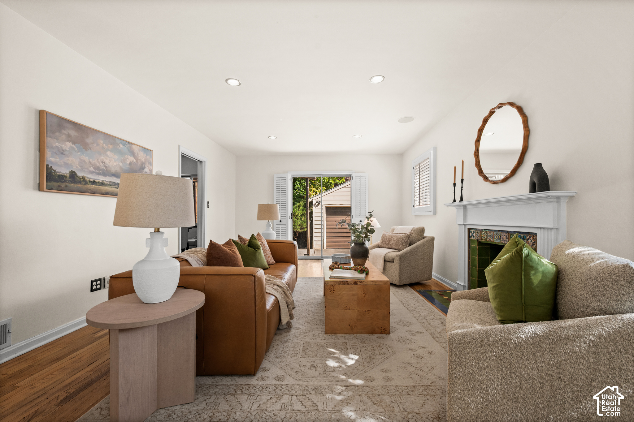 Staged living room with brown leather sofa and white fireplace with colorful tile surround.