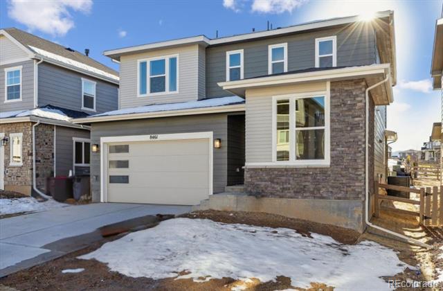 Two-story gray and stone-sided house with a white garage door and snow in the front yard.