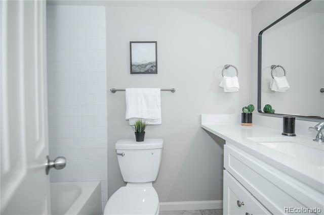 Bathroom with a white vanity and large mirror, toilet beneath a towel bar, and partially visible bathtub.