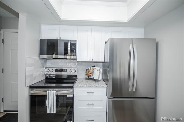 Kitchen with white cabinetry, stainless steel appliances, gray counters, and a bright recessed ceiling feature.