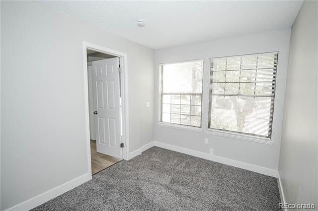 Empty bedroom with gray carpet, two windows with blinds, and an open doorway.