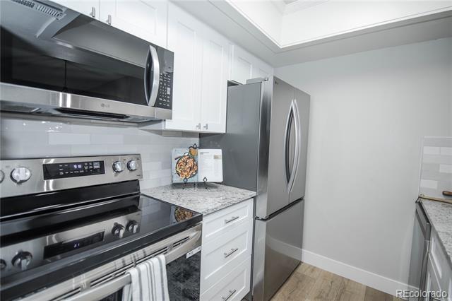 Kitchen with white cabinetry, stainless steel appliances, patterned countertops, and wood-look flooring.