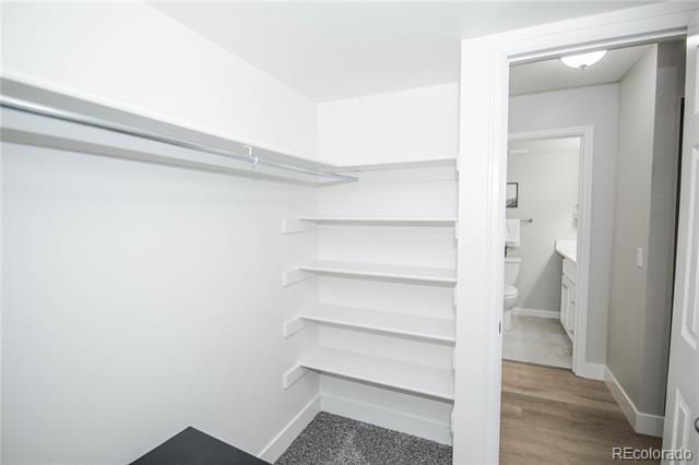 Walk-in closet with white shelving and a hanging rod beside an open bathroom doorway.
