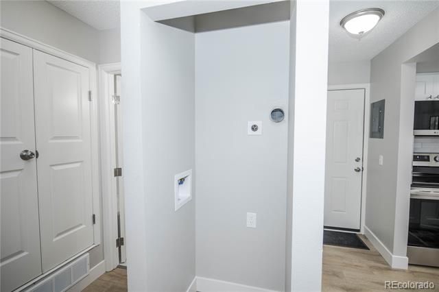 Recessed laundry area with utility connections beside the condo entryway and kitchen.
