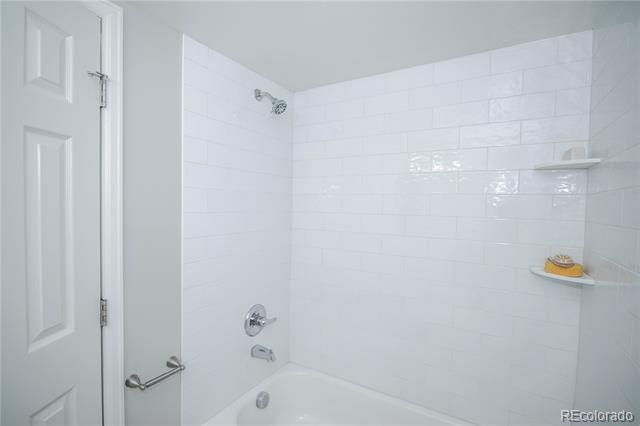 White-tiled tub and shower with chrome fixtures and built-in corner shelves.
