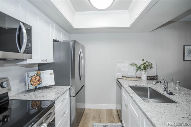 Kitchen with white cabinets, stainless steel appliances, marble-patterned counters, and a large skylight.