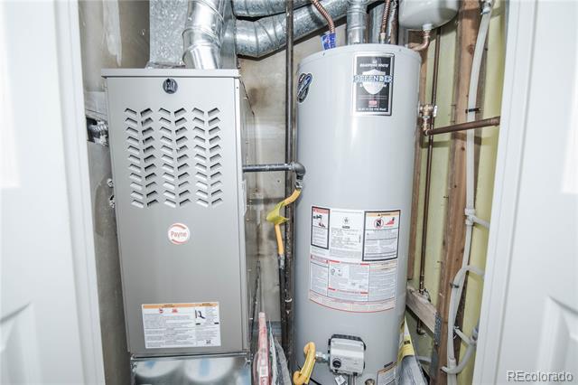 Utility area with a Payne furnace and water heater beneath exposed ductwork and pipes.