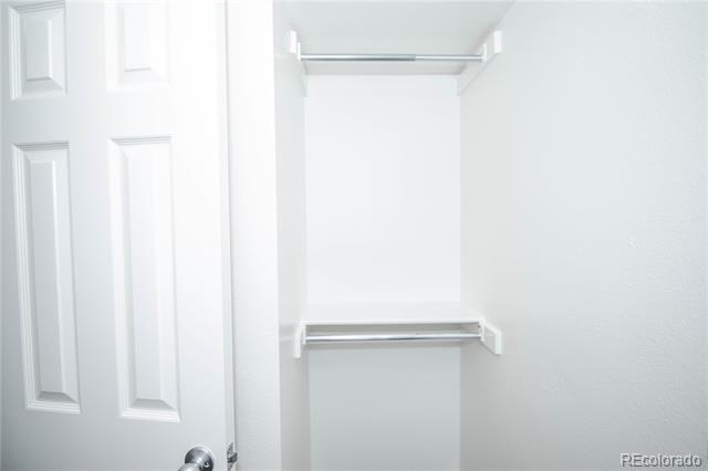 Empty white closet with two hanging rods and a small shelf.