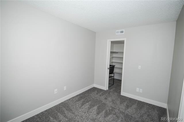 Empty carpeted bedroom with a doorway to a small closet with built-in shelves.