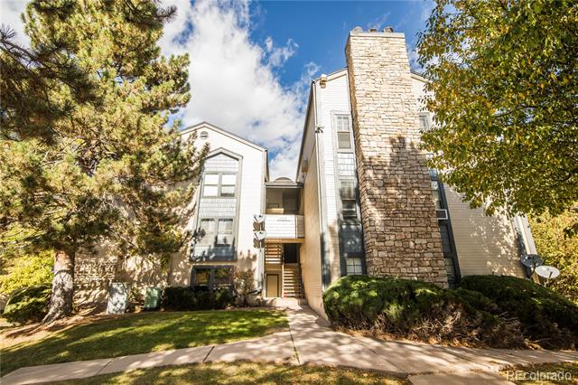 Condominium building with a tall stone chimney, balconies, and trees framing the entrance.