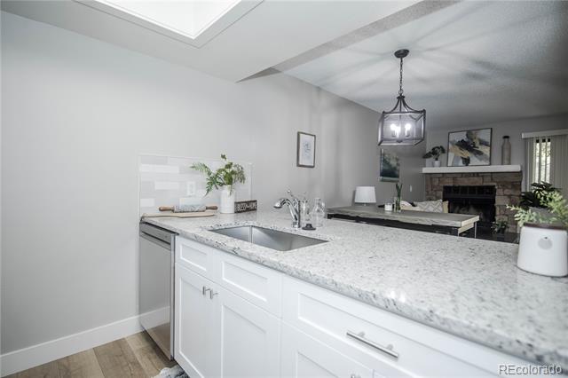 White kitchen peninsula with a speckled stone counter and sink overlooks a living room fireplace.