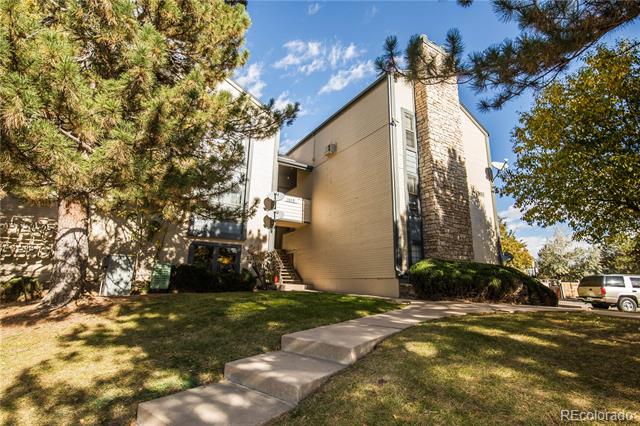 Multi-unit residential building with a stone-faced section, balconies, and a walkway through the lawn.