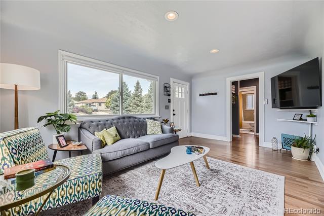 Living room with a gray tufted sofa, patterned chairs, large window, and hardwood floors.