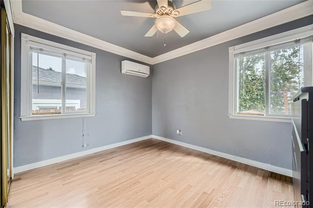 Empty bedroom with light wood flooring, gray walls, two windows, and a ceiling fan.
