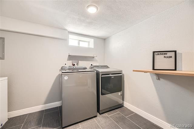 Laundry room with a washer and dryer, dark tile flooring, and a narrow wall shelf.