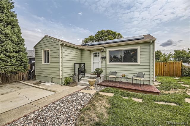 Sage-green single-story house with solar panels, a front porch, and a stone path.