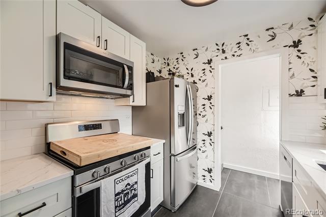 Kitchen with white cabinetry, stainless-steel appliances, gray tile flooring, and black floral wallpaper.