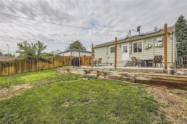 House backyard with a raised wooden deck, patio seating, and a broad lawn.
