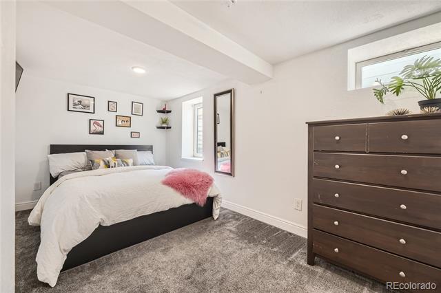 Bedroom with a white bed, pink throw, dark dresser, and gray carpet.