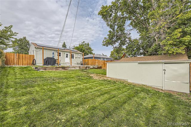 Backyard with a broad grassy lawn, wooden privacy fence, and long white storage shed.