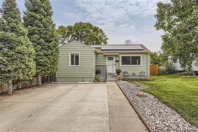 Pale green single-story house with rooftop solar panels and a broad concrete driveway.