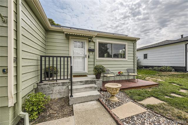 Pale green home entrance with concrete steps, black railing, and a small patio with chairs.