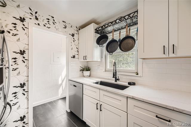 Bright white kitchen with hanging pans, floral wallpaper, and a sink beneath the window.