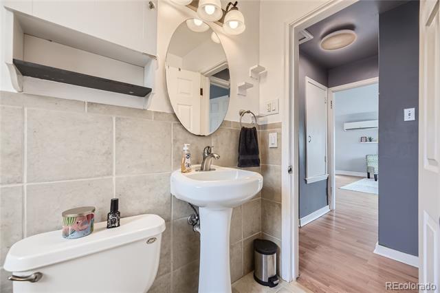 Bathroom with a pedestal sink and toilet beside an open doorway to a wood-floored room.