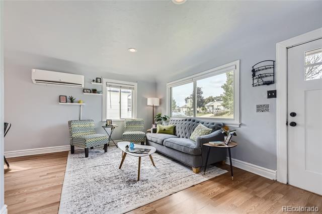 Living room with a gray tufted sofa, patterned chairs, large windows, and light wood floors.