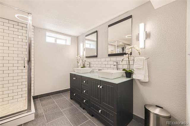 Bathroom with a gray double vanity, vessel sinks, and a glass-enclosed subway-tile shower.