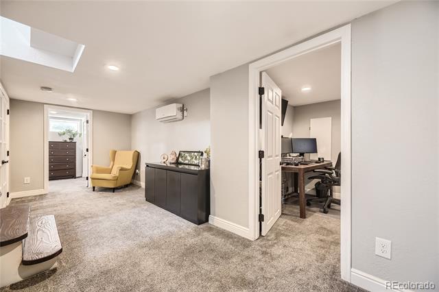 Carpeted bonus room with a yellow armchair and an open doorway to a home office.