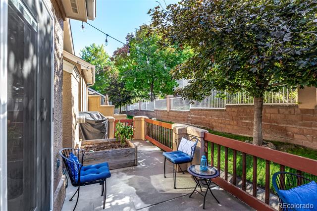 Patio with blue chairs, a small table, raised planter, and mature trees.