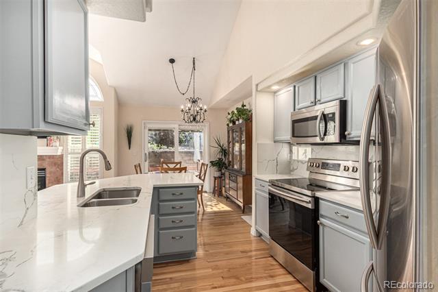 Bright kitchen with a white island, gray cabinets, stainless steel appliances, and wood floors.
